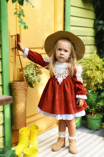 Beautiful little girl of two years old playing in the autumn yard. Little child playing in the yard of the house. Girl with long hair in a dress