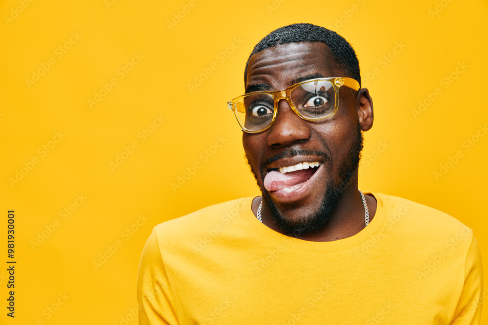 Smiling young man with glasses making a funny face on a bright yellow background, wearing a yellow shirt, conveying happiness and playfulness in a vibrant setting
