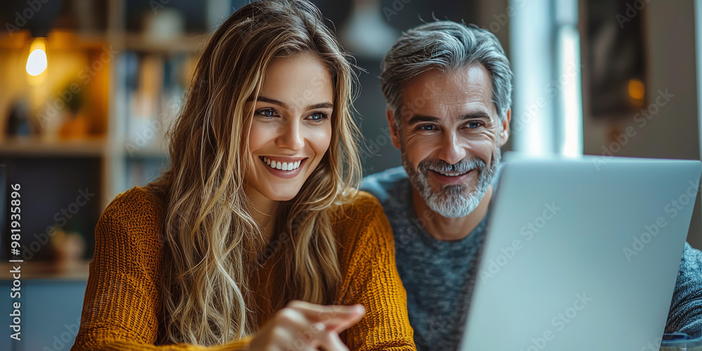 Fototapeta premium A young woman and a mature man are looking at a laptop screen while smiling.