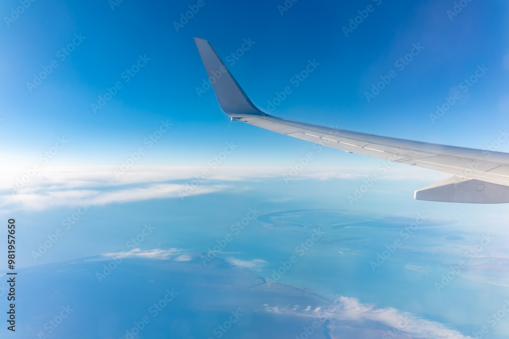View from the airplane window at a beautiful blue clear sky, earth, sea and the airplane wing