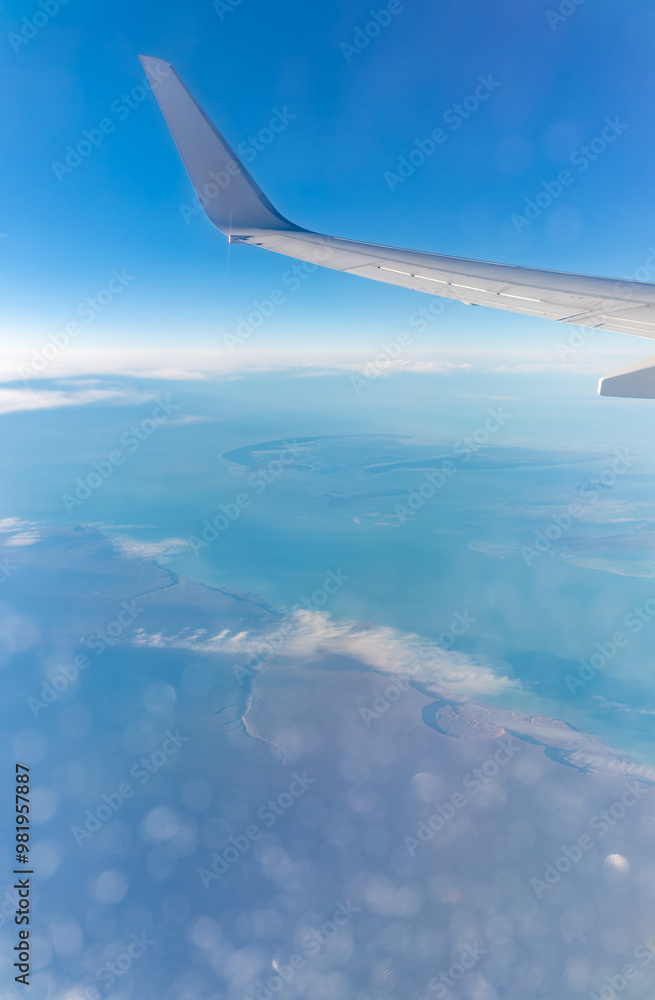 Obraz premium View from the airplane window at a beautiful blue clear sky, earth, sea and the airplane wing