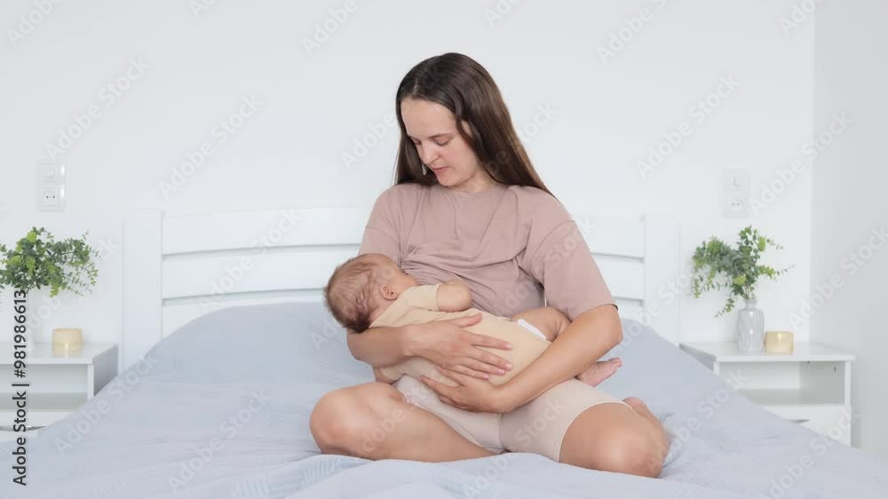 Young mother spending time with her baby son or daughter child embracing and hugging kid sitting on the bed and breastfeeding baby lulling her infant kid in light bedroom interior Young mother spending time with her baby son or daughter child embracing and hugging kid sitting on the bed and breastfeeding baby lulling her infant kid in light bedroom interior