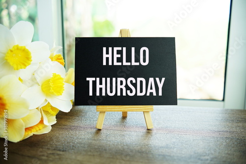 Hello Thursday text message with wooden easel and flower bouquet on wooden background photo