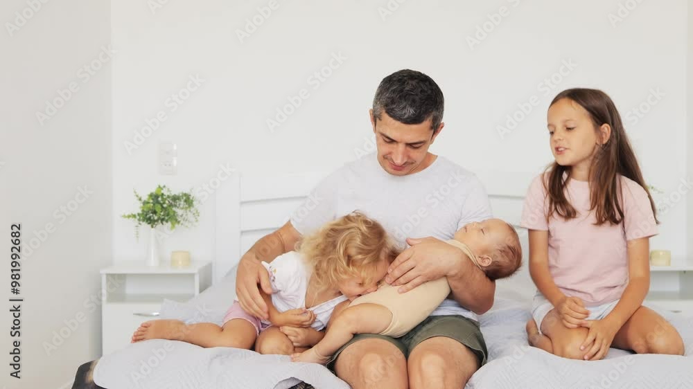 Happy delighted smiling man with children affectionately soothing baby sharing joyful moments together with his kids tricking children family posing in bright cozy interior of bedroom Happy delighted smiling man with children affectionately soothing baby sharing joyful moments together with his kids tricking children family posing in bright cozy interior of bedroom