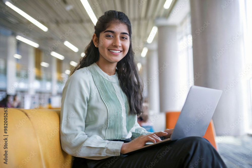 Indian college girl in casual formals with laptop in modern library