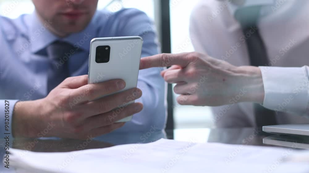 colleague at work points to a file in a partner's smartphone