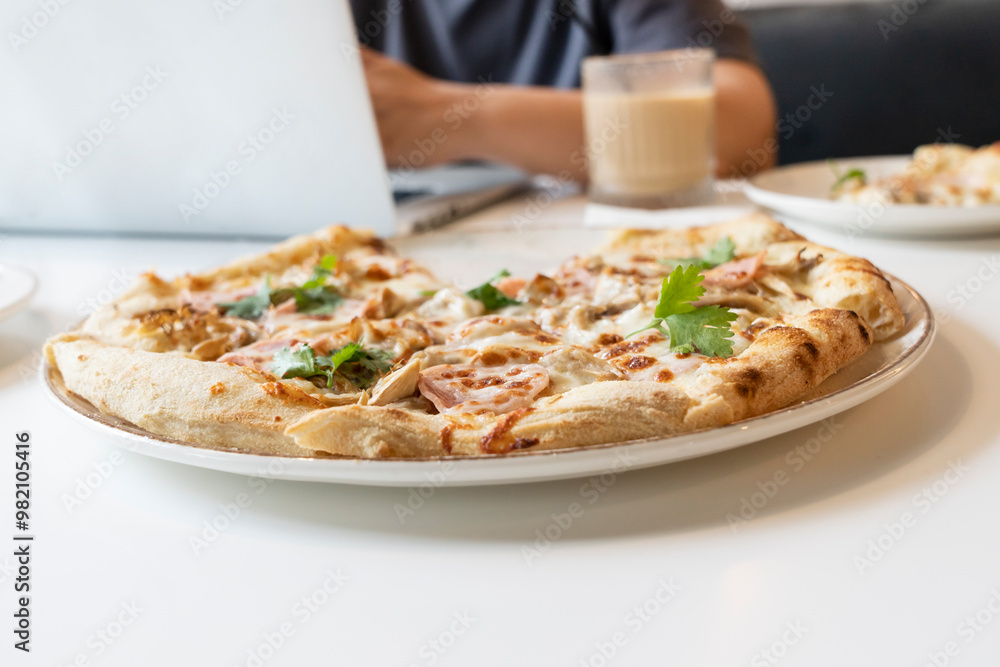 Close-up photo of delicious pizza and man working on laptop on the background in the cafe Close-up photo of delicious pizza and man working on laptop on the background in the cafe