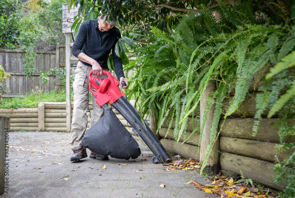 Man working with a leaf vacuum in the backyard. Auckland.
