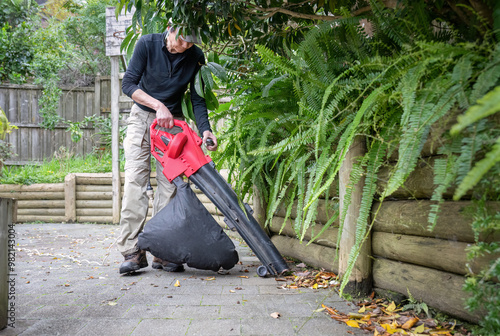 Obraz na płótnie Man working with a leaf vacuum in the backyard. Auckland. w salonie