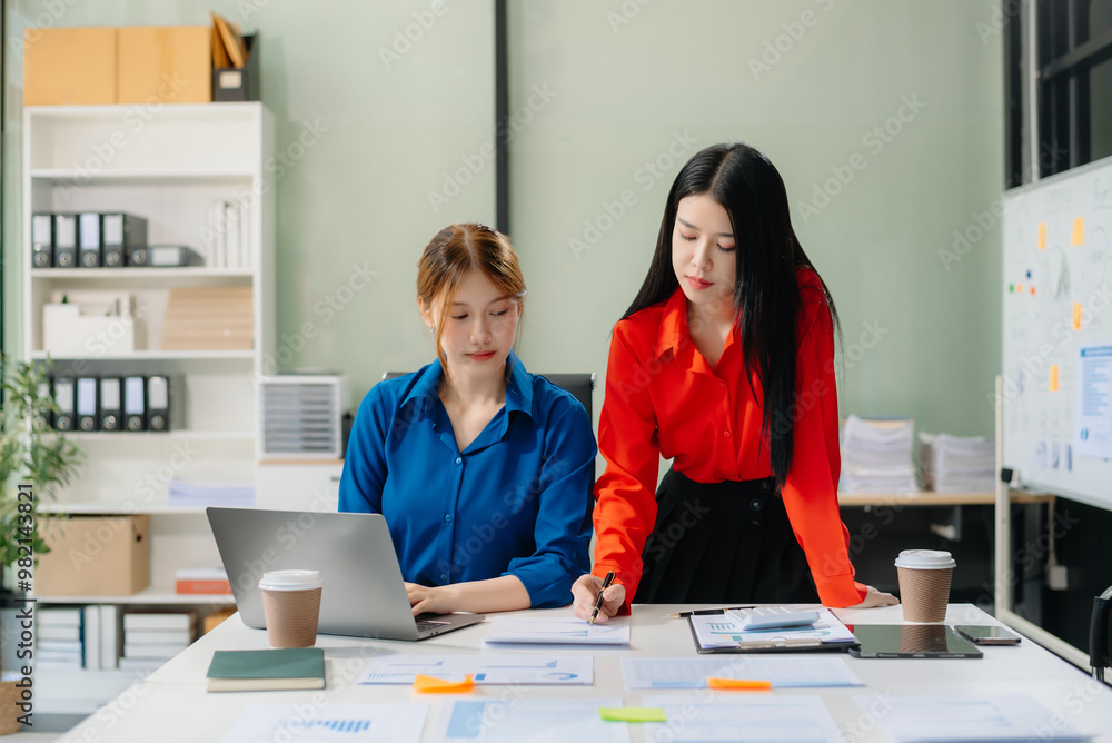Two young Asian professionals engaged in teamwork and business discussions in modern office Two young Asian professionals engaged in teamwork and business discussions in modern office
