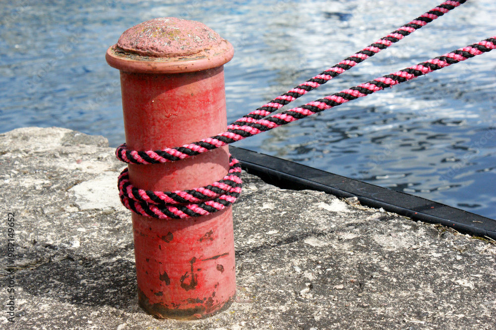 Red sailing hawser mooring rope from yacht in the port on concrete quay Red sailing hawser mooring rope from yacht in the port on concrete quay