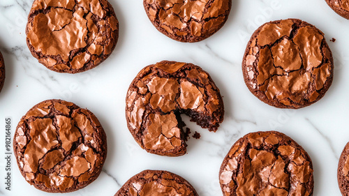 Vista desde arriba de varias galletas de brownie de chocolate sobre una superficie de mármol blanco, con una galleta partida por la mitad para revelar el interior blando y meloso