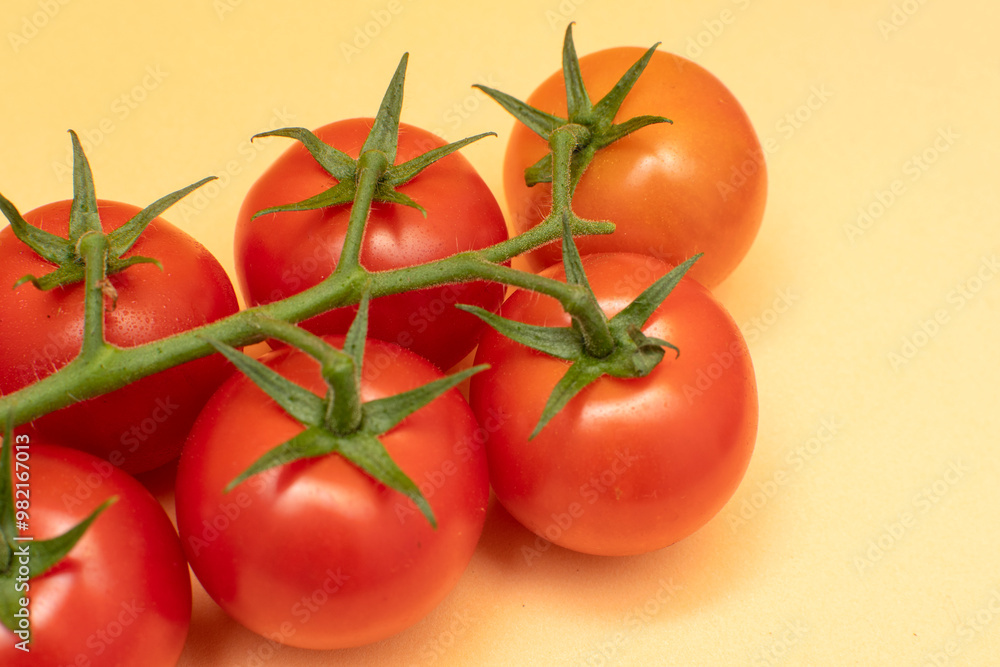 Red cherry tomatoes with green branch on yellow background Red cherry tomatoes with green branch on yellow background