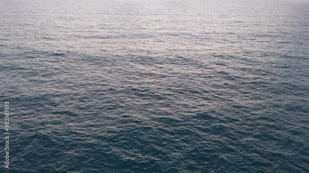 Slow-motion drone shot over ocean waves at sunrise. Colors of blue and orange fill the sky as clouds rise on the horizon. Various angles capture the sea’s movement. Slow-motion drone shot over ocean waves at sunrise. Colors of blue and orange fill the sky as clouds rise on the horizon. Various angles capture the sea’s movement.