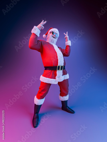 Santa claus showing rock and roll hand gesture posing under neon lights
