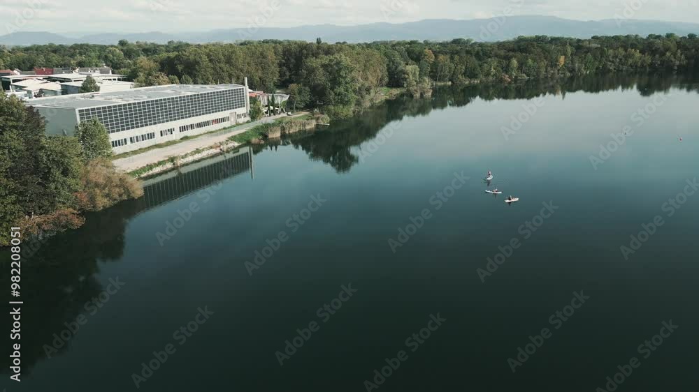 Drone flies diagonally over beautiful lake in germany with SUP Stand-Up Paddlers in the middle and trees come in view Drone flies diagonally over beautiful lake in germany with SUP Stand-Up Paddlers in the middle and trees come in view
