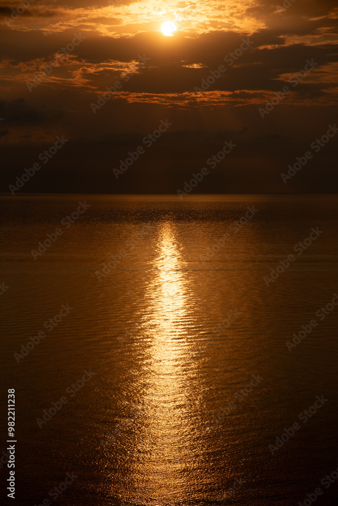 Fototapeta premium Golden sunset reflecting on calm ocean water with dramatic clouds