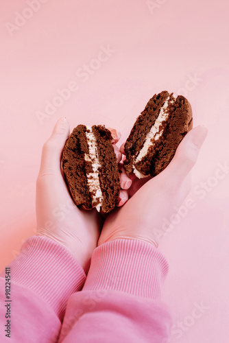 Brownie Cookies with Cream Cheese cut in half in woman's hands on pink background photo