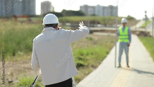 Surveyor with an optical level waves his hand to control colleagues from a distance