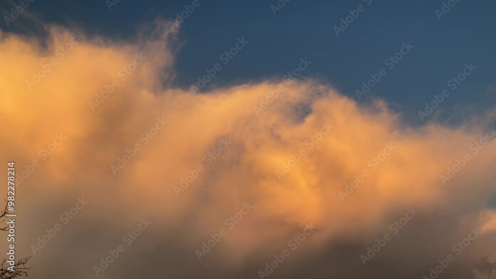 Blue sky with stormy menacing Anvil cloud, Cumulonimbus incus illuminated in orange by sunlight at the evening - shot with camera movement. Topics: storm alert, meteorology, weather, nature, climate Blue sky with stormy menacing Anvil cloud, Cumulonimbus incus illuminated in orange by sunlight at the evening - shot with camera movement. Topics: storm alert, meteorology, weather, nature, climate