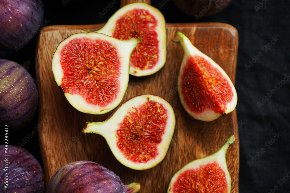 Ripe whole and sliced figs on a wooden board on a dark background Ripe whole and sliced figs on a wooden board on a dark background