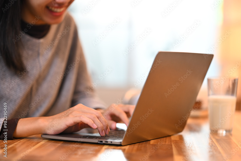 Smiling young woman sitting at kitchen counter with a glass of milk and working with laptop Smiling young woman sitting at kitchen counter with a glass of milk and working with laptop