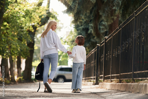 Rear view, walking. Schoolgirl with her mother are outdoors together