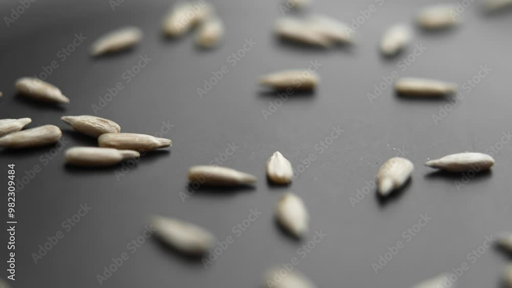 Peeled raw sunflower seeds falling in slow motion on black matte ceramic surface Peeled raw sunflower seeds falling in slow motion on black matte ceramic surface