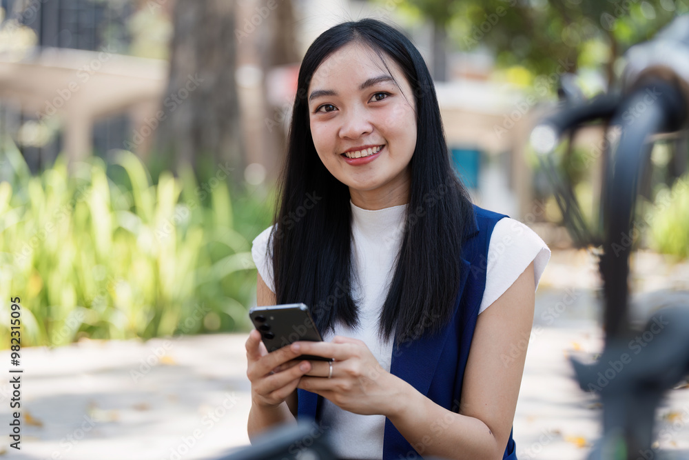 Young Woman Smiling While Using Smartphone Outdoors in Urban Park Setting on a Sunny Day Young Woman Smiling While Using Smartphone Outdoors in Urban Park Setting on a Sunny Day