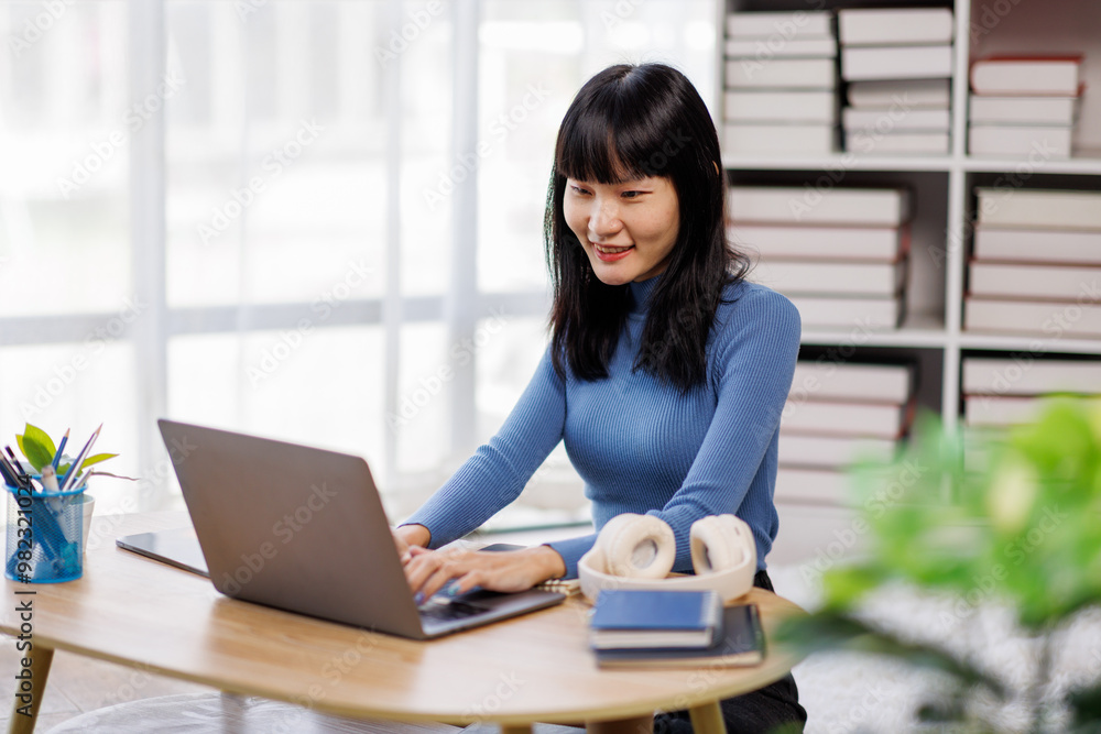 Happy asian woman using laptop while working remotely from home in living room Happy asian woman using laptop while working remotely from home in living room