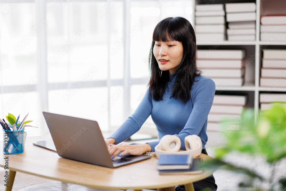 Happy asian woman using laptop while working remotely from home in living room Happy asian woman using laptop while working remotely from home in living room