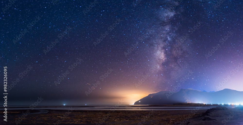 Naklejka premium A serene night sky illuminates the coastal mountains. The Milky Way stretches across the horizon, casting a soft glow over the tranquil seascape. Suao, Yilan County, Taiwan.