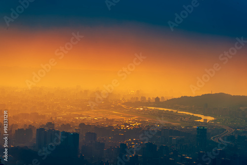 A panoramic view of Taipei City after the rain, with the Keelung River winding through the urban landscape. The setting sun casts a warm glow over the cityscape. Taipei, Taiwan.