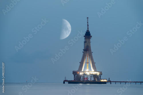 A serene night scene of the Tamsui Bridge under construction with a crescent moon in the sky. The soft glow of the construction lights contrasts beautifully with the calm waters, Taiwan. photo