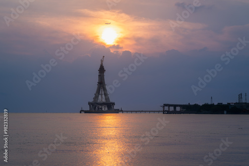 A majestic silhouette of the Tamsui Bridge under construction is bathed in the golden hues of sunset. The unfinished structure stands tall against a vibrant sky. Tamsui, Taiwan.