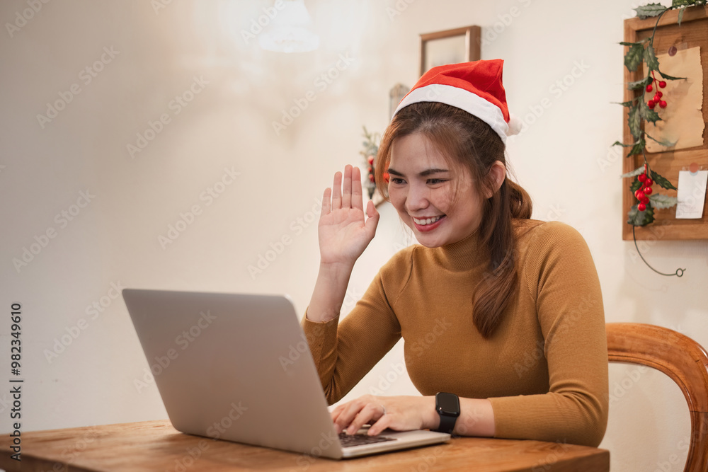 Young Woman Video Calling on Christmas Day, Wearing Santa Hat, Smiling and Waving, Celebrating Holiday Season Virtually with Family and Friends Young Woman Video Calling on Christmas Day, Wearing Santa Hat, Smiling and Waving, Celebrating Holiday Season Virtually with Family and Friends