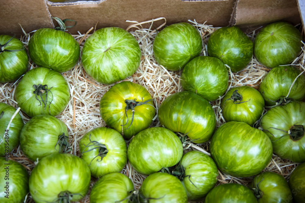 Closeup of fresh vibrant green heirloom tomatoes in a carton cardboard box at local farmers market. Assorted organic heirloom beef tomatoes. Healthy eating, gardening, and farm-to-table concept. Top Closeup of fresh vibrant green heirloom tomatoes in a carton cardboard box at local farmers market. Assorted organic heirloom beef tomatoes. Healthy eating, gardening, and farm-to-table concept. Top