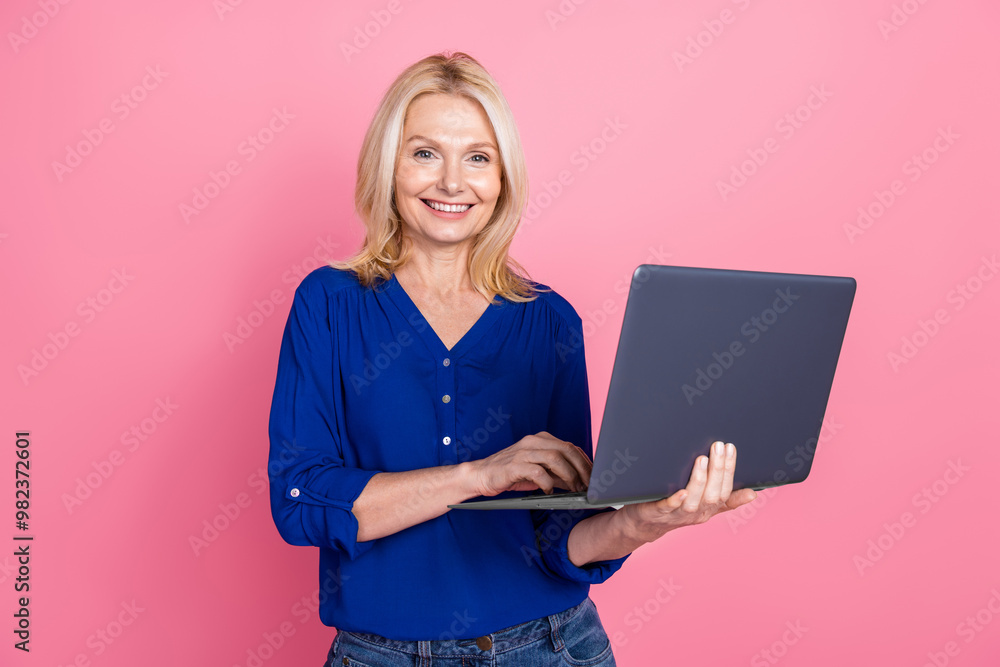 Photo portrait of attractive retired woman hold netbook dressed stylish blue clothes isolated on pink color background Photo portrait of attractive retired woman hold netbook dressed stylish blue clothes isolated on pink color background