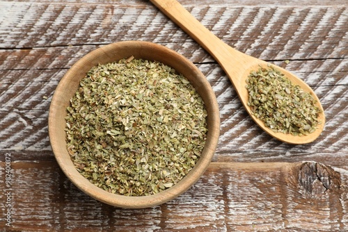 Dried oregano in bowl and spoon on wooden table, top view