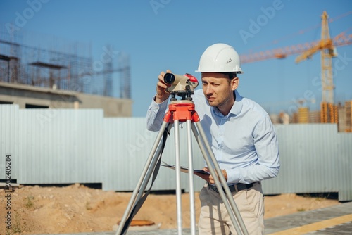 Civil Engineer Foreman in white protective helmet using level equipment. Surveyor s level at construction site at work. photo