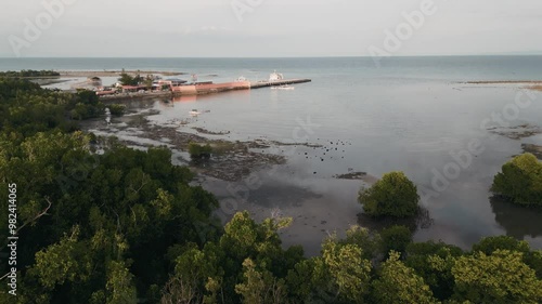 Dramatic aerial overview of Taloot Argao Port at sunrise, showing the bustling maritime activity in Cebu, Philippines, tilt up with clouds reflecting in water photo