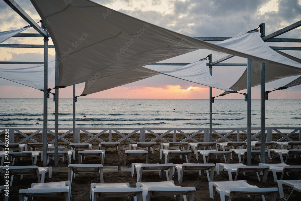 Late cool evening, sunset over the beach on the seashore, closing of the season, empty sun loungers Late cool evening, sunset over the beach on the seashore, closing of the season, empty sun loungers
