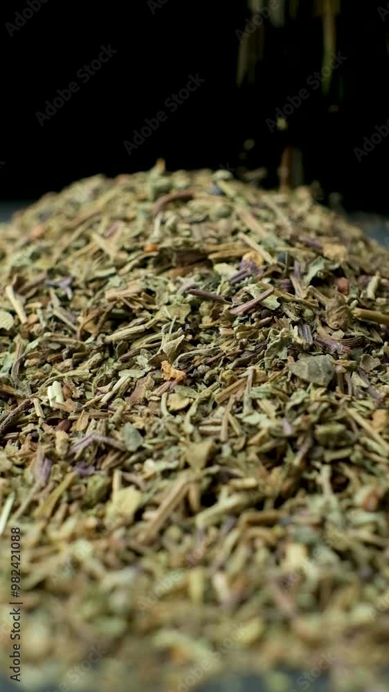 Basil seasoning is pouring and spinning, black background, vertical slow motion Basil seasoning is pouring and spinning, black background, vertical slow motion