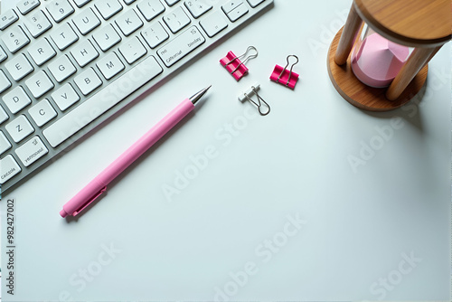 A computer keyboard, a pen, and an hourglass are resting on a white table