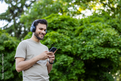 Smiling man in park using smartphone and headphones for music and fitness inspiration