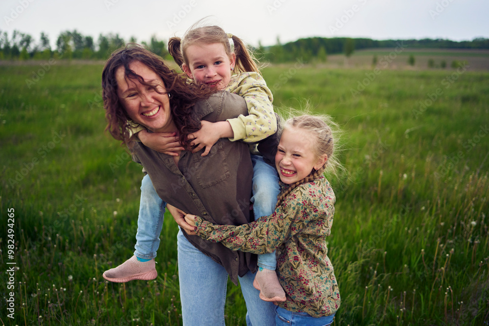 a mother rolls her daughters on her back, playing horse, kisses and hugs a mother rolls her daughters on her back, playing horse, kisses and hugs