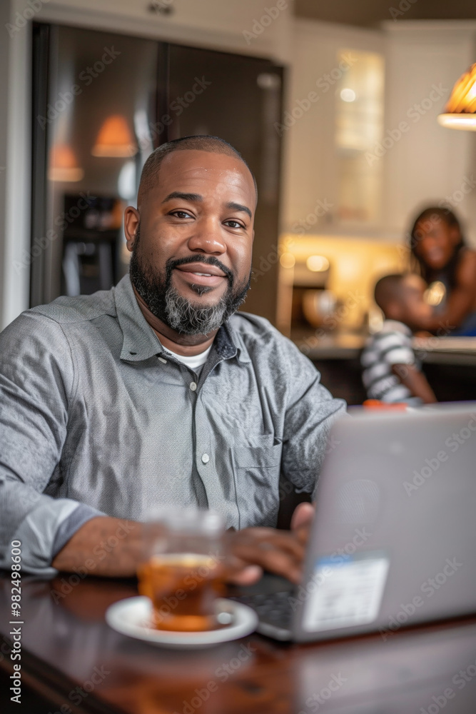 Smiling man working on laptop at home with family in the background Smiling man working on laptop at home with family in the background