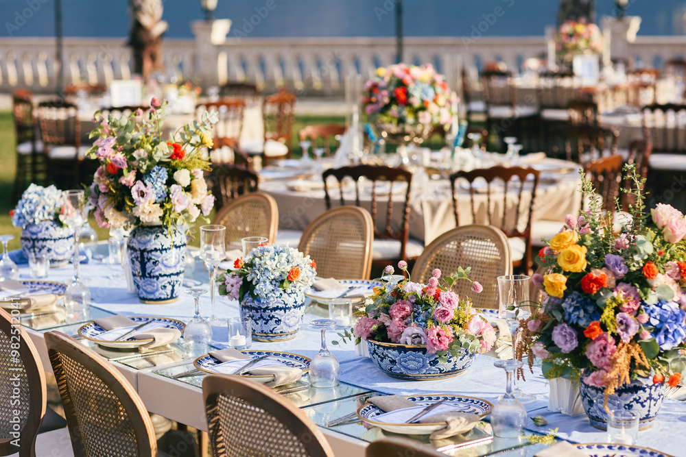 A romantic and elegant wedding tablescape with floral arrangements in blue and white porcelain vases, and gold accents, set against a breathtaking coastal view