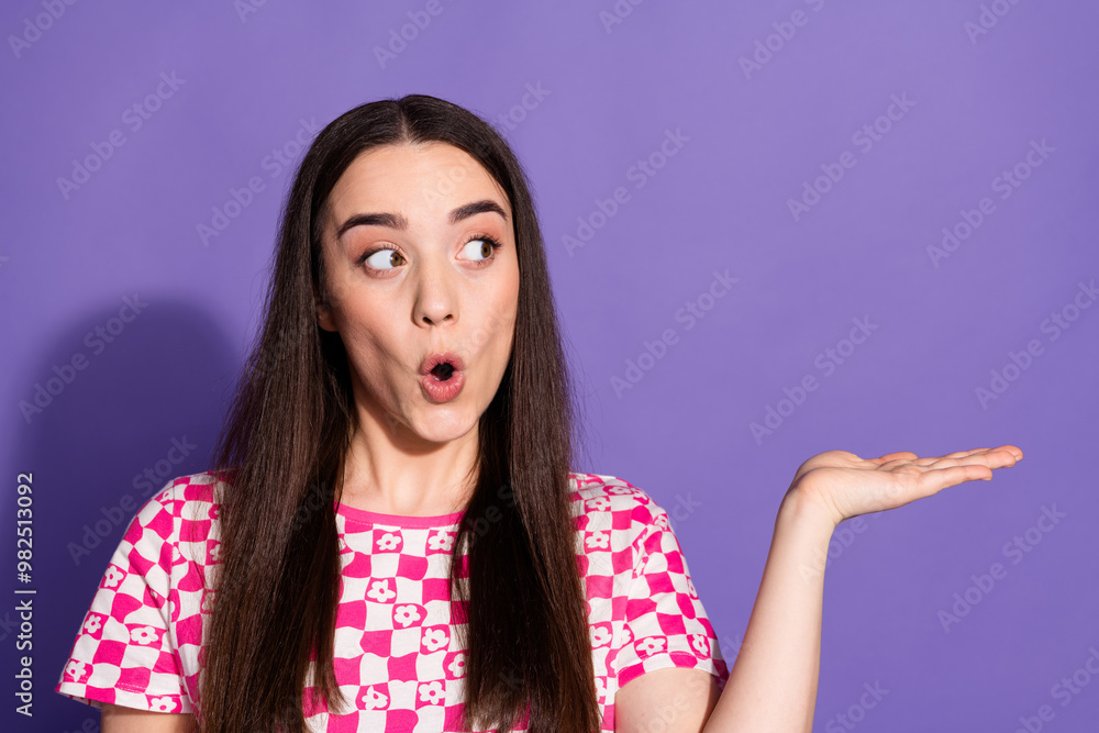 Portrait of nice young woman look hold empty space wear checkered t-shirt isolated on violet color background Portrait of nice young woman look hold empty space wear checkered t-shirt isolated on violet color background