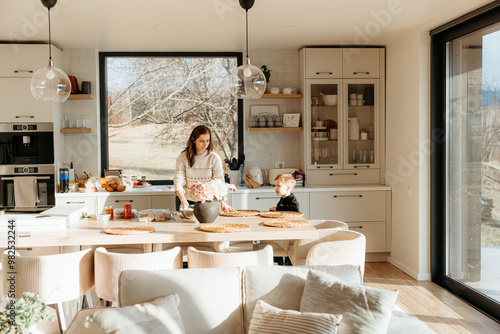 Mother arranging flowers in modern sunny kitchen preparing lunch with son